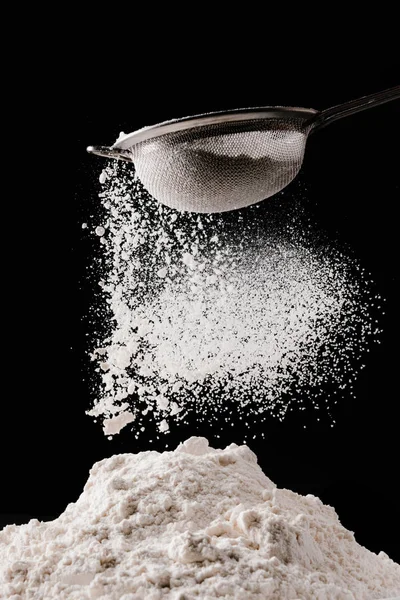 Flour falling from sieve on pile isolated on black — Stock Photo