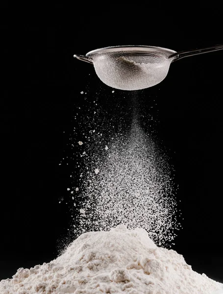 Flour falling from sieve on pile isolated on black — Stock Photo