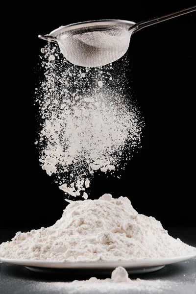 Mehl fällt aus Sieb auf Stapel, isoliert auf schwarz — Stockfoto