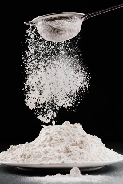 Flour falling from sieve on pile isolated on black — Stock Photo