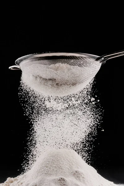 White flour falling from sieve on pile isolated on black — Stock Photo