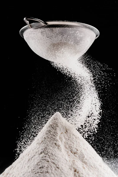 White flour falling from sieve on pile isolated on black — Stock Photo