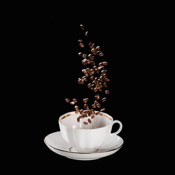 Chicchi di caffè che cadono in tazza isolata su nero — Foto stock