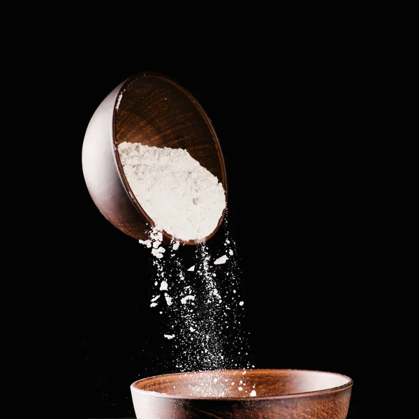 Bowl with falling flour into another bowl isolated on black — Stock Photo