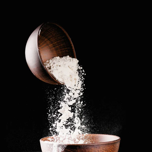 Bowl with falling flour into another bowl isolated on black — Stock Photo