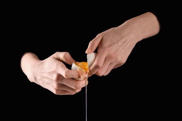 Cropped image of woman holding broken dripping chicken egg in hands isolated on black — Stock Photo