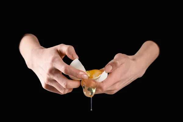 Cropped image of woman holding broken chicken egg isolated on black — Stock Photo