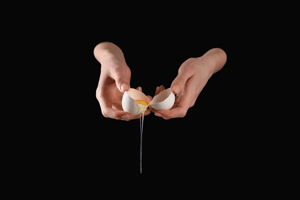 Cropped image of woman holding broken dripping chicken egg isolated on black — Stock Photo