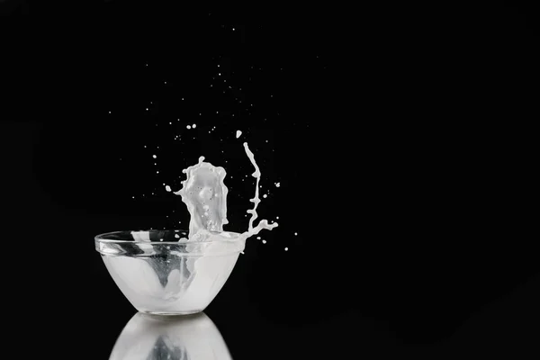 Milk pouring out from bowl on black reflecting tabletop — Stock Photo