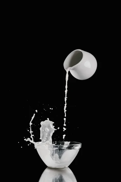 Milk pouring from milk jar into bowl on black — Stock Photo