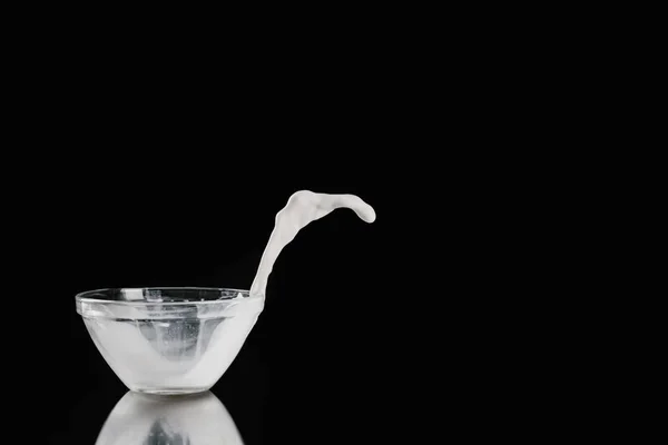 Milk pouring out from bowl on black reflecting table — Stock Photo