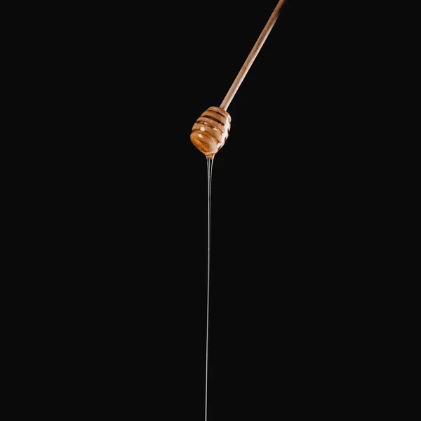 Apetecible miel goteo de miel palo aislado en negro - foto de stock