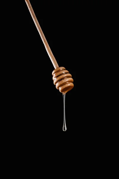 Honey dripping from honey stick isolated on black — Stock Photo