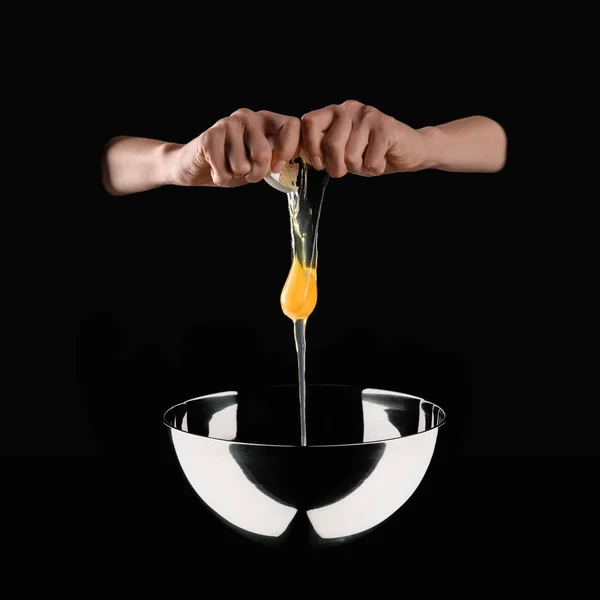 Cropped image of woman putting broken chicken egg into bowl solated on black — Stock Photo