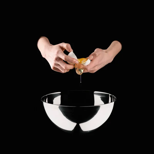 Cropped image of woman holding broken chicken egg above bowl isolated on black — Stock Photo
