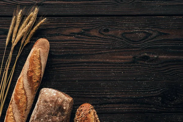 Top view of arranged loafs of bread and wheat on wooden surface — Stock Photo