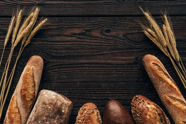 Vista superior de los panes y el trigo dispuestos en la superficie de madera - foto de stock