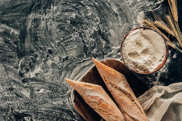 Vista superior de piezas dispuestas de baguette francés y trigo en la mesa oscura con harina - foto de stock