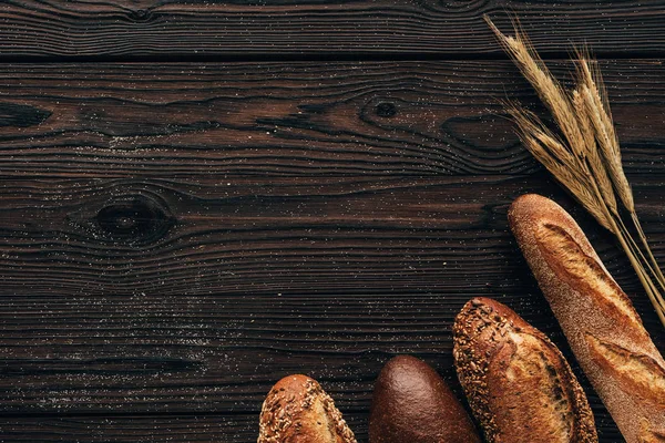 Top view of arranged loafs of bread and wheat on wooden surface — Stock Photo