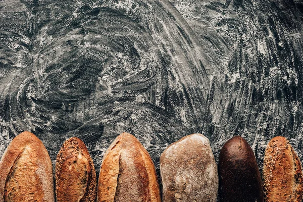 Top view of arranged loafs of bread on dark tabletop with flour — Stock Photo