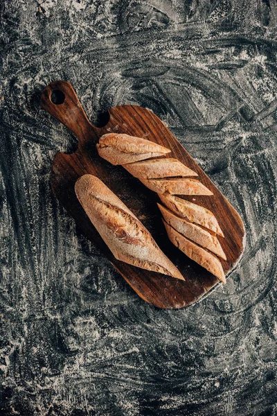 Vista dall'alto di pezzi disposti di baguette francese sul tagliere su superficie scura con farina — Foto stock