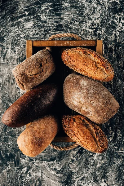 Vista superior de loafs arranjados de pão em caixa de madeira em mesa escura com farinha — Fotografia de Stock