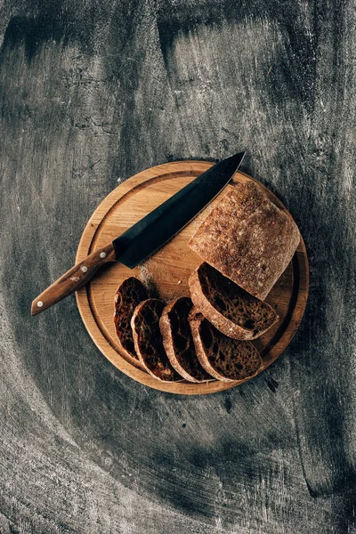 Ansicht von angeordneten Brotstücken auf Schneidebrett mit Messer auf dunkler Oberfläche mit Mehl — Stockfoto