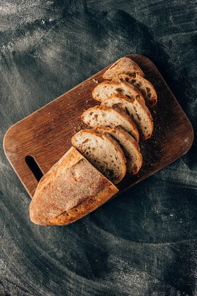 Vista superior de pedaços arranjados de pão na tábua de corte na superfície escura com farinha — Fotografia de Stock