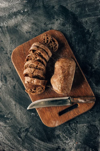 Top view of arranged pieces of bread on cutting board with knife on dark surface with flour — Stock Photo