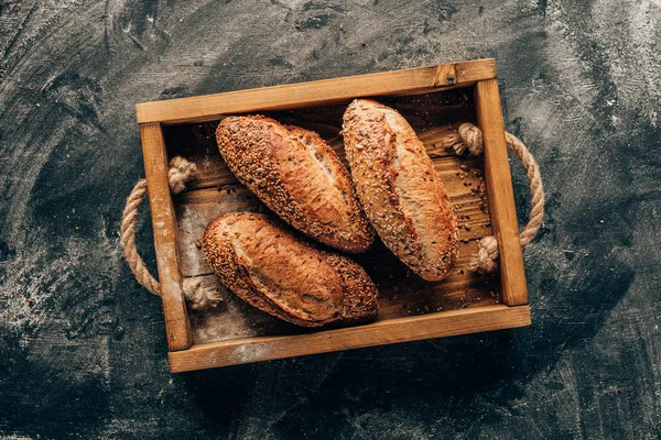 Top view of arranged loafs of bread in wooden box on dark tabletop with flour — Stock Photo