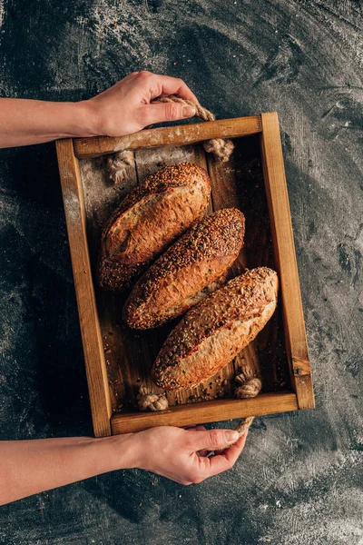 Cropped shot of woman holding wooden box with loafs of bread in hands — Stock Photo