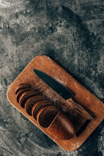 Top view of arranged pieces of bread on cutting board with knife on dark surface with flour — Stock Photo