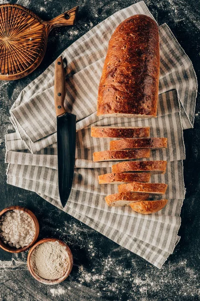 Flat lay with pieces of bread on linen and bowls with flour near by on dark tabletop — Stock Photo