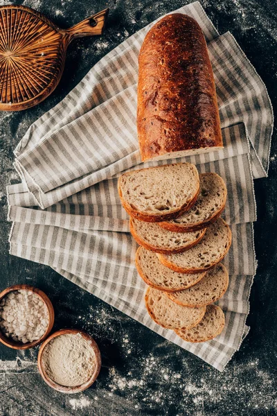 Deitado com pedaços de pão em linho e tigelas com farinha perto de mesa escura — Fotografia de Stock