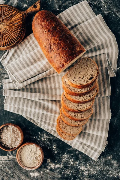 Flat lay with pieces of bread on linen and bowls with flour near by on dark tabletop — Stock Photo