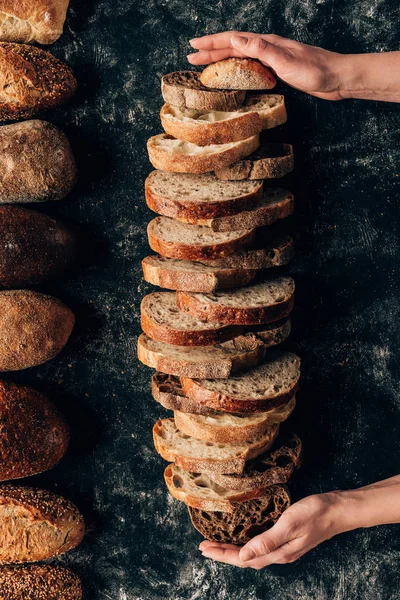 Tiro cortado de mãos femininas e pedaços arranjados de pão na mesa escura — Fotografia de Stock