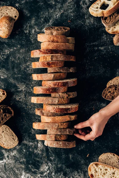 Cropped shot of female hand and arranged pieces of bread on dark surface with flour — Stock Photo