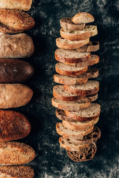 Top view of arranged loafs and pieces of bread on dark tabletop — Stock Photo