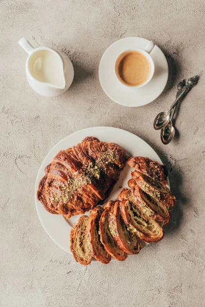 Acostado plano con jarra de leche, taza de café y croissants dulces con nueces de pistacho en el plato en la mesa ligera - foto de stock