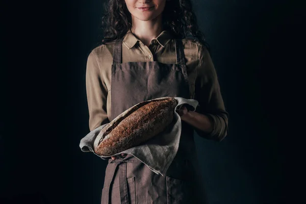 Partial view of woman in apron holding french baguette in hands isolated on black — Stock Photo