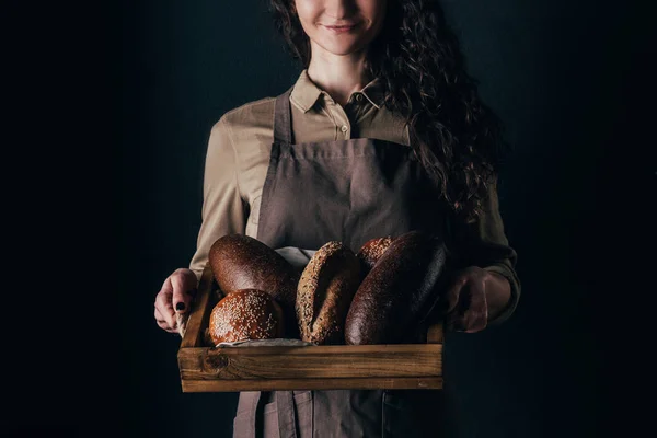 Foto recortada de mujer sonriente sosteniendo caja de madera con panecillos en las manos aisladas en negro - foto de stock