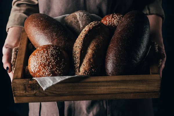 Cropped shot of woman holding wooden box with loafs of bread in hands — Stock Photo