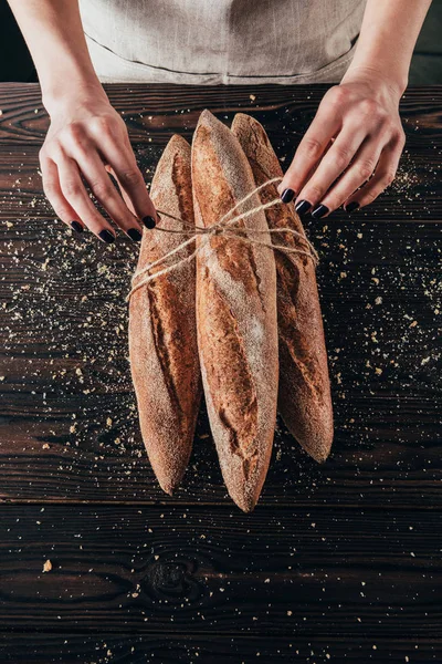 Vue partielle de la femme attachant une corde autour des baguettes françaises sur une surface en bois — Photo de stock