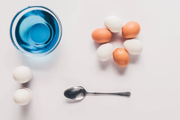 Vista dall'alto di vetro con vernice blu e uova di pollo con cucchiaio su superficie bianca, concetto di Pasqua — Foto stock