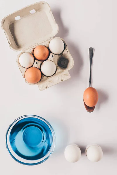 Vista superior de vidrio con pintura azul y huevos de pollo en bandeja de huevo, concepto de Pascua - foto de stock