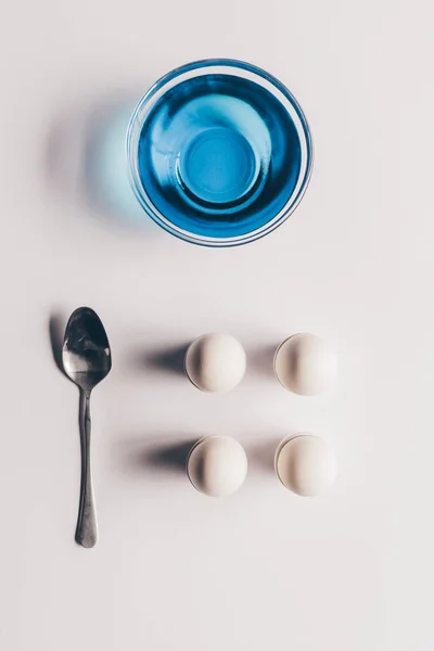 Vista dall'alto di vetro con vernice blu e uova di pollo con cucchiaio su superficie bianca, concetto di Pasqua — Foto stock