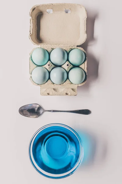 Vue du dessus du verre avec peinture bleue, cuillère et oeufs de poulet dans le plateau, concept de Pâques — Photo de stock