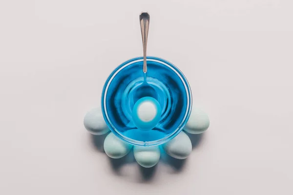 Vue du dessus de l'oeuf en verre avec peinture bleue et oeufs de poulet sur la surface blanche, concept de Pâques — Photo de stock