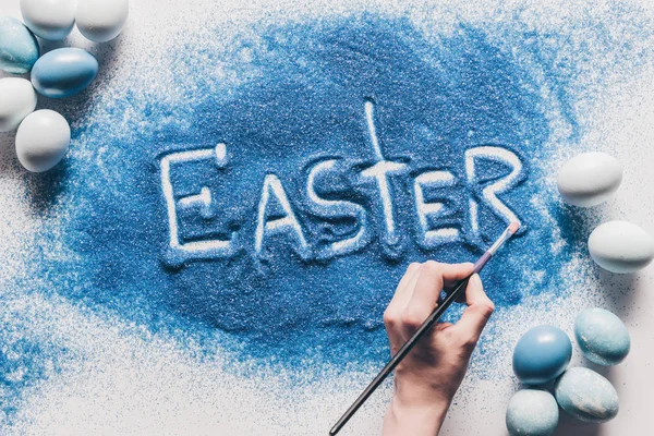 Cropped image of woman making easter sign with blue sand on white surface — Stock Photo