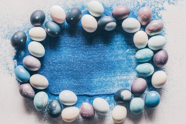 Vue de dessus des œufs de Pâques peints et du sable bleu sur la surface blanche — Photo de stock